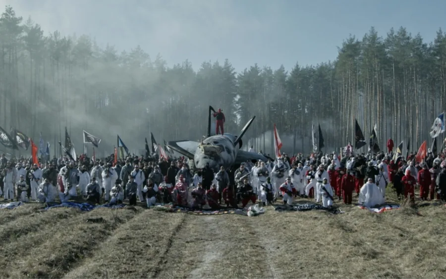 Film still from GOD HATES SPACE by GENER8ION, presented by Art Basel and Live Nation: a crowd with flags around a wrecked aircraft in a misty forest clearing